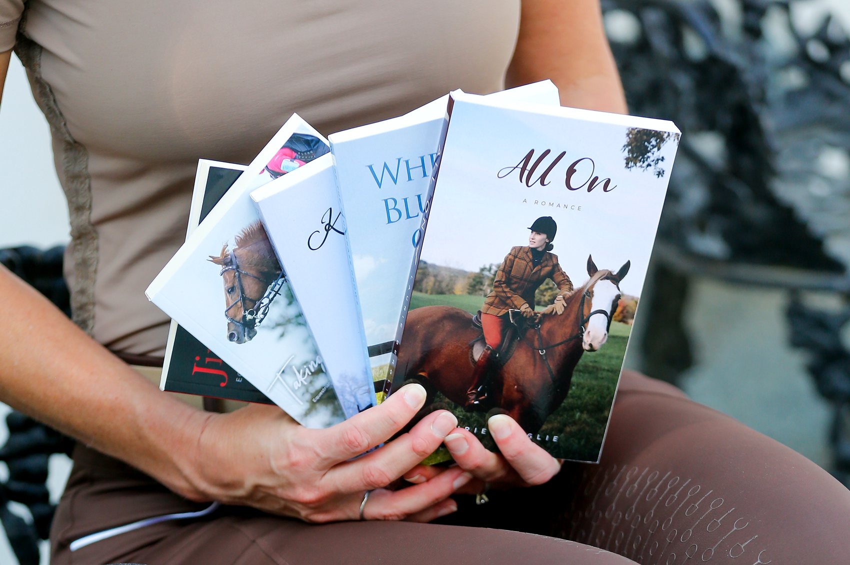 Laurie Berglie holding a fan of her signed paperbacks: Where the Bluegrass Grows, Kicking On, Taking Off, Jingle Horse and All On